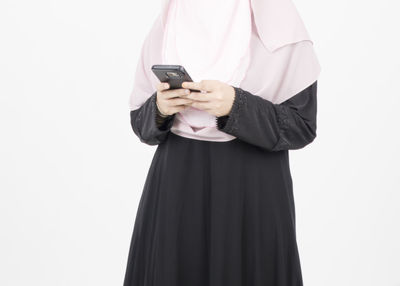 Midsection of woman holding mobile phone against white background