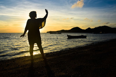 Woman standing on beach against sky during sunset