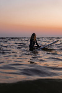 Silhouette person in sea against sky during sunset