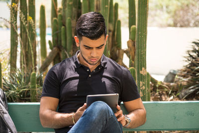Portrait of man using digital tablet on park bench