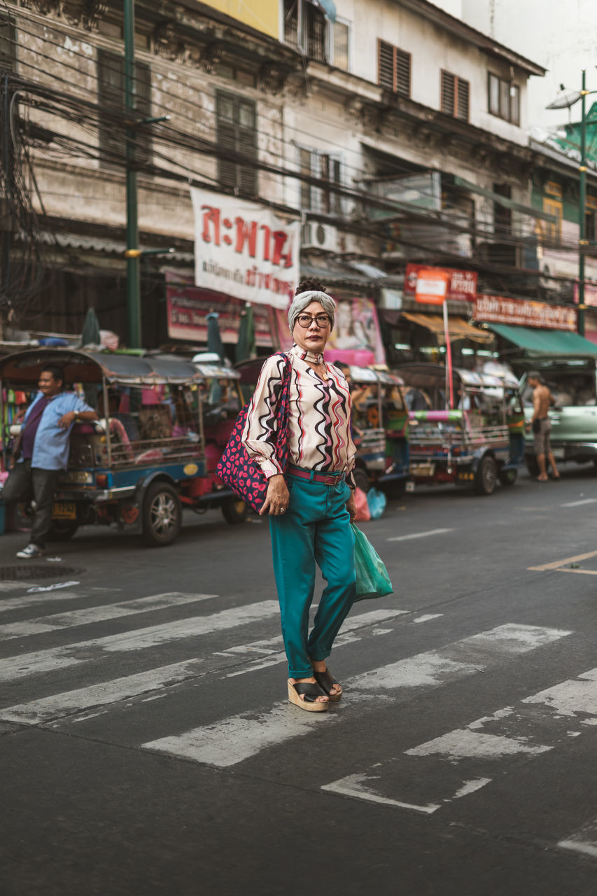 city, street, architecture, building exterior, transportation, full length, car, built structure, motor vehicle, one person, road, mode of transportation, casual clothing, incidental people, walking, city life, lifestyles, crossing, day, city street, outdoors