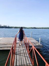 Rear view of woman standing at river against sky