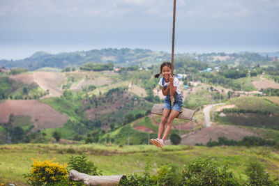 Full length of girl swinging against landscape