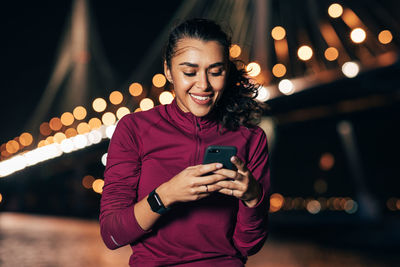Portrait of smiling young woman using mobile phone at night