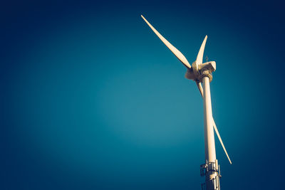 Low angle view of wind turbine against clear blue sky