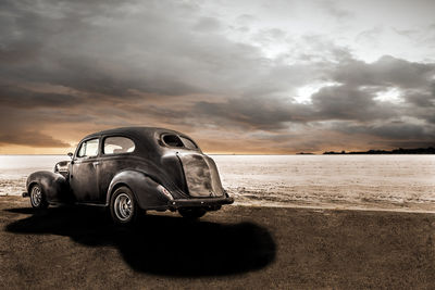 Vintage car at beach against cloudy sky during sunset