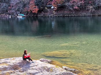 Side view of woman sitting on rock by lake