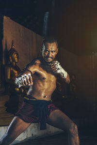 Shirtless mid adult man practicing muay thai at night