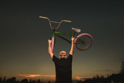 Man with arms raised standing against sky during sunset