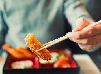 Midsection of man holding meat with chopsticks in restaurant