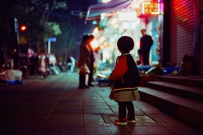 Rear view of girl standing on footpath at night