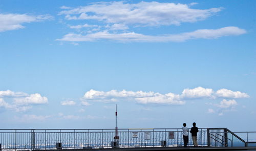 People standing by railing against sea