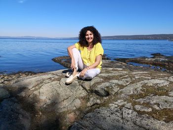 Portrait of woman sitting on rock against sea