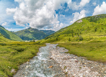 Scenic view of stream amidst green landscape against sky