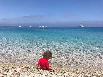 Rear view of playful girl sitting on shore at beach against sky