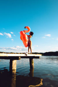 Rear view of woman sitting on pier over sea against sky