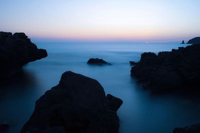 Rock formation in sea against sky during sunset