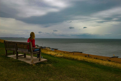 Woman sitting on bench by sea against sky