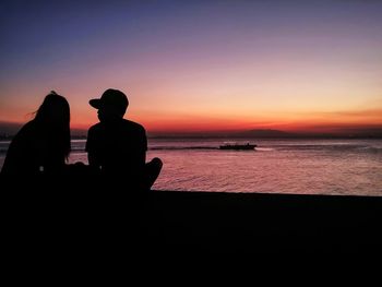 Silhouette people sitting on beach against sky during sunset