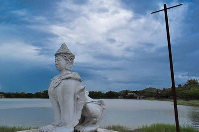 Statue by lake against sky