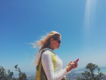 Side view of woman using mobile phone against blue sky