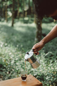 Cropped hand of man pouring coffee in glass on field