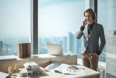 Businessman talking over mobile phone while standing by window