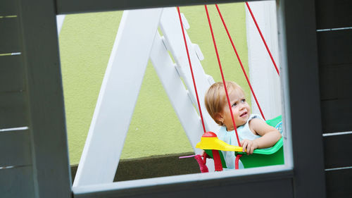 Summer, in the garden, nice little one year-old girl swinging on a swing in the playground.