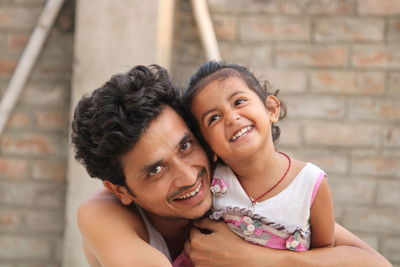 Portrait of happy father holding daughter against brick wall