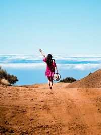 Back-shot of a young woman going forward by country road to the horizon with a raised hand