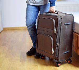 Low section of person holding luggage while standing at home