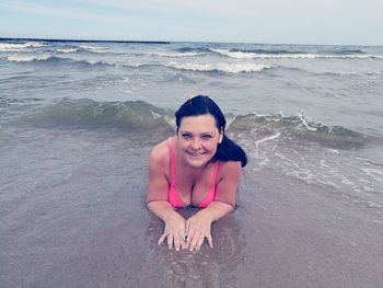 Portrait of smiling young woman lying at beach against sky