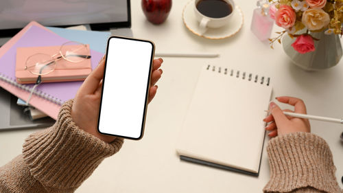 Cropped hand of woman using mobile phone on table