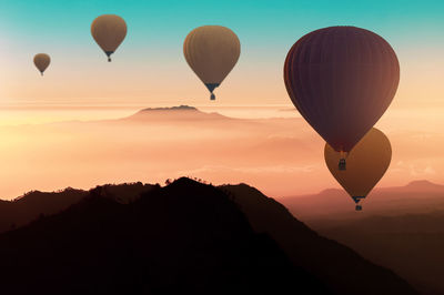 Hot air balloons flying over silhouette mountains against sky during sunset
