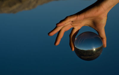 Midsection of person holding ball in blue sky