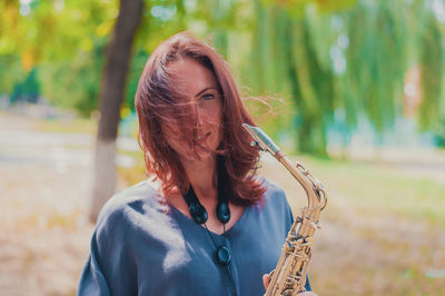 Beautiful red-haired girl in a blue jacket with a saxophone in windy weather