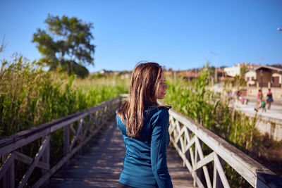 Rear view of woman walking on footbridge against clear blue sky