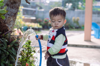 Adorable asian toddler boy plays and enjoys having fun watering garden flowers and lawn 