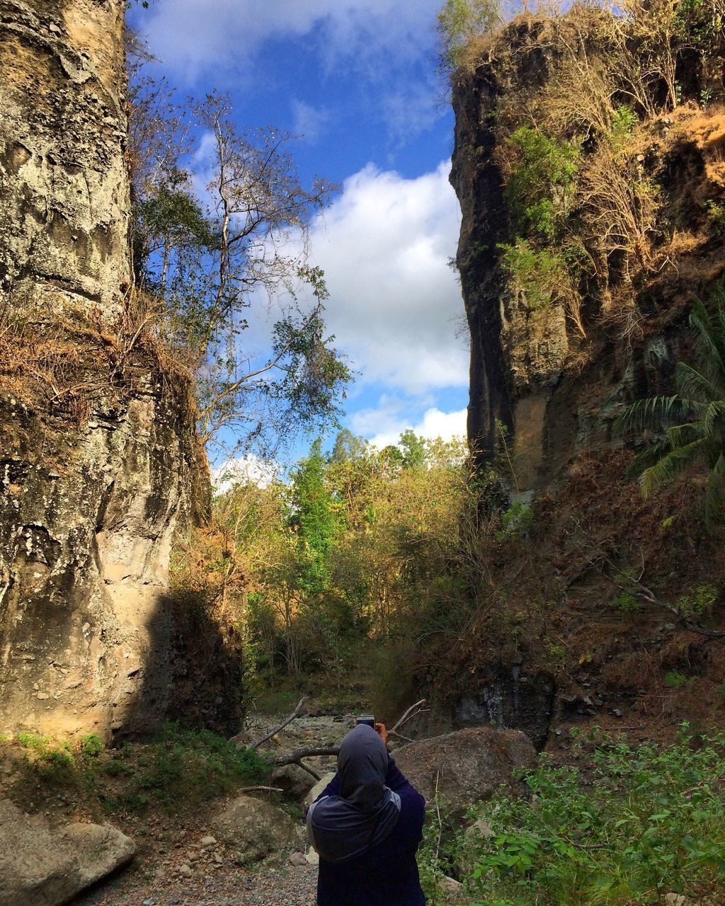 REAR VIEW OF MAN STANDING ON ROCK AGAINST SKY