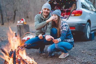 Couple embracing while sitting by bonfire at forest