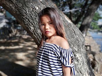 Portrait of young woman standing against tree trunk