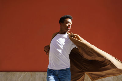 Young man looking away while standing against red wall