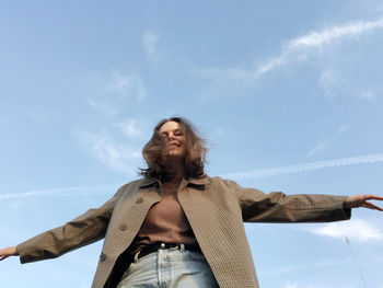 Low angle view of smiling young woman looking away against sky