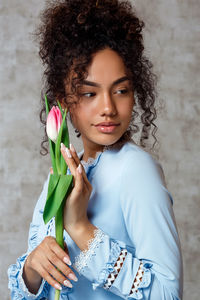 Beautiful young woman holding flower looking away at home