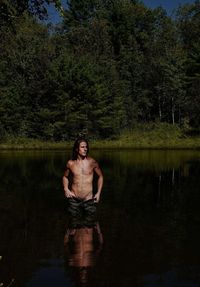 Shirtless man standing in lake against trees