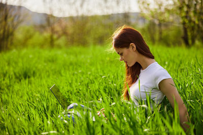 Side view of young woman sitting on grassy field