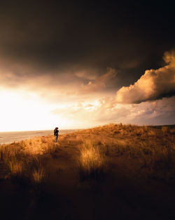 Distant view of woman standing at beach against sky during sunset