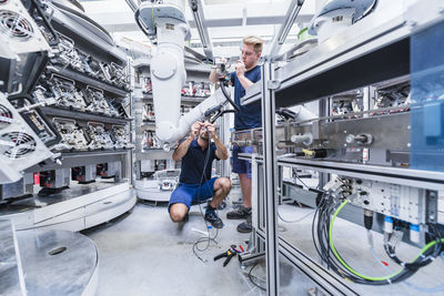 Two colleagues working at industrial robot in modern factory