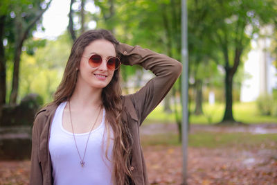 Portrait of smiling beautiful woman wearing sunglasses against trees