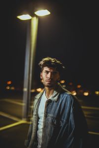 Young man standing against illuminated light at night